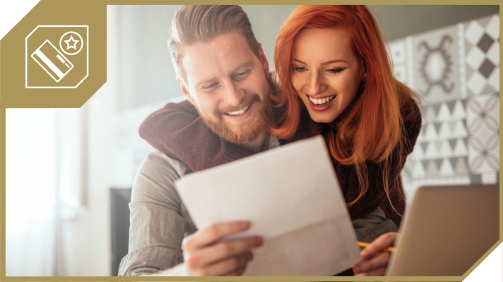 Na sliki je nasmejan par, ki skupaj gledata račun za elektriko. Moški v ospredju drži list, medtem ko se dekle smeje in ju ovija toplo svetloba domačega okolja.