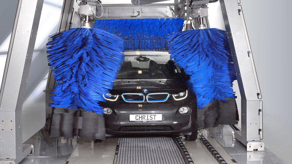 "Na sliki je črn BMW v sodobni avtomatski avtopralnici. Velike modre krtače čistijo avto iz lev, desne in zadnje strani.