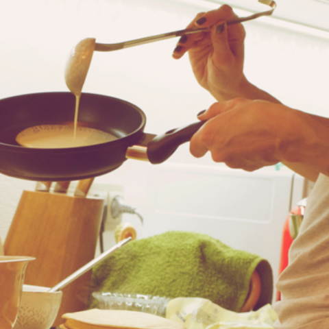 Na sliki oseba z zajemalko vliva maso za palačinke v ponev na štedilniku.