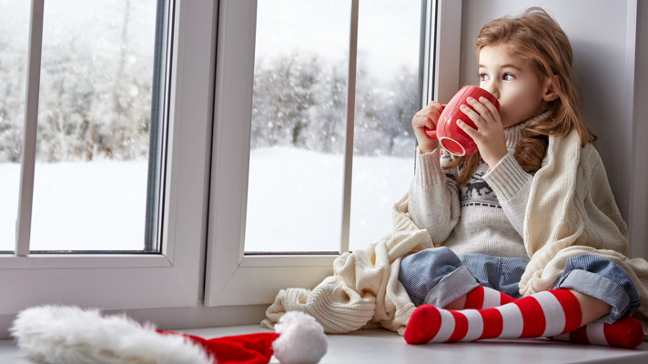 Na sliki je deklica, ki sedi ob oknu, zavita v odejo in gleda ven zasneženo zimsko pokrajino. Iz rdeče skodelice pije topel napitek, ob njej pa na tleh leži božična kapa.