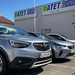 Parkirana srebrna vozila pred poslovalnico ATET rent a car, z belo-modro tablo ATET v ozadju.