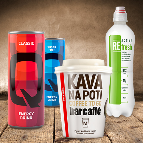 Petrol napitki – pločevinka Q Energy Drink, steklenica REfresh in lonček kave na poti Barcaffè, postavljeni na leseno ozadje.