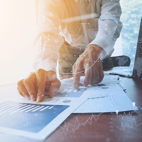Oseba v poslovni srajci s svinčnikom v roki pregleduje dokumente z grafi in tabelami, na sliko so dodani digitalni grafični elementi, ki ponazarjajo analizo in rast poslovanja.