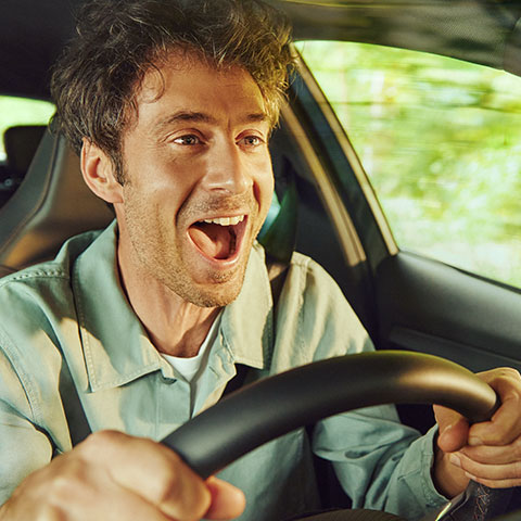 Moški z nasmehom sedi za volanom avtomobila in uživa v vožnji.