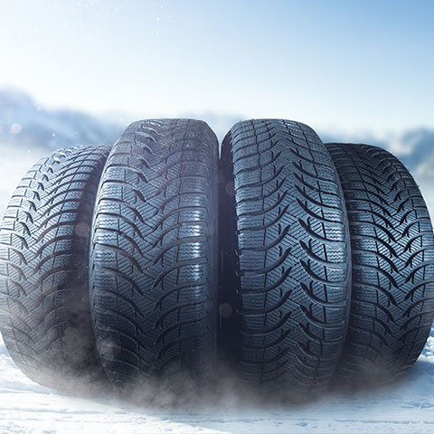 Štiri zložene zimske pnevmatike na snežni podlagi s svetlim ozadjem.