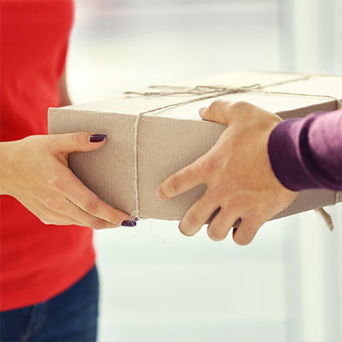 Oseba v rdeči majici izroča paket drugi osebi, ki ga prevzema z obema rokama.