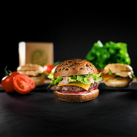 Svež hamburger s solato in paradižnikom kot del Petrolove ponudbe hrane, na črnem ozadju.