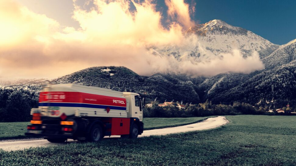 Na sliki je Petrolov tovornjak cisterna za dostavo kurilnega olja, ki vozi po podeželski cesti z zasneženimi gorami v ozadju.