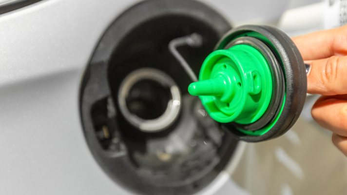 Na sliki je odprt rezervoar avtomobila, v katerega nekdo drži zelen pokrovček za gorivo.