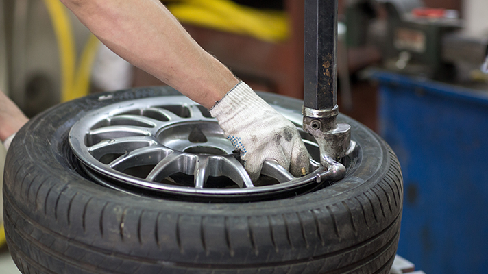 Na sliki je mehanik, ki z orodjem namešča pnevmatiko na aluminijasto platišče.