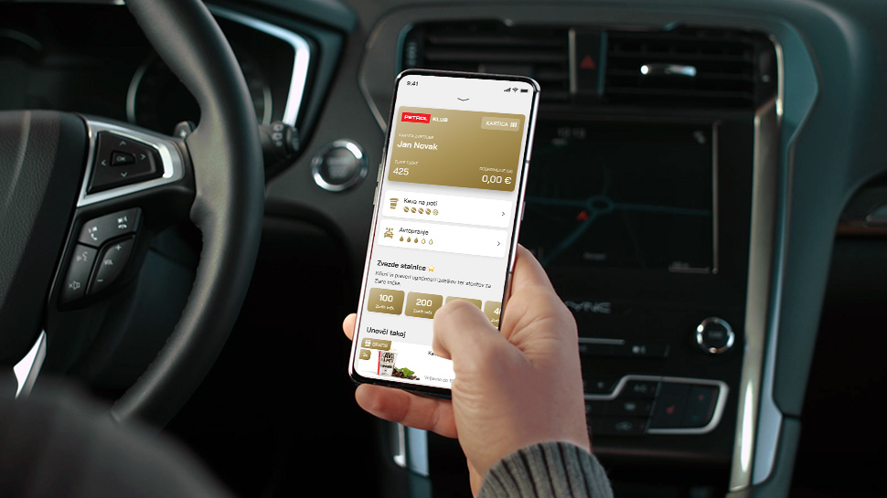 Oseba v avtomobilu drži telefon z odprto aplikacijo Petrol, kjer so prikazani zbrani zvestobni podatki, kartica in ugodnosti v sklopu Perol klub.