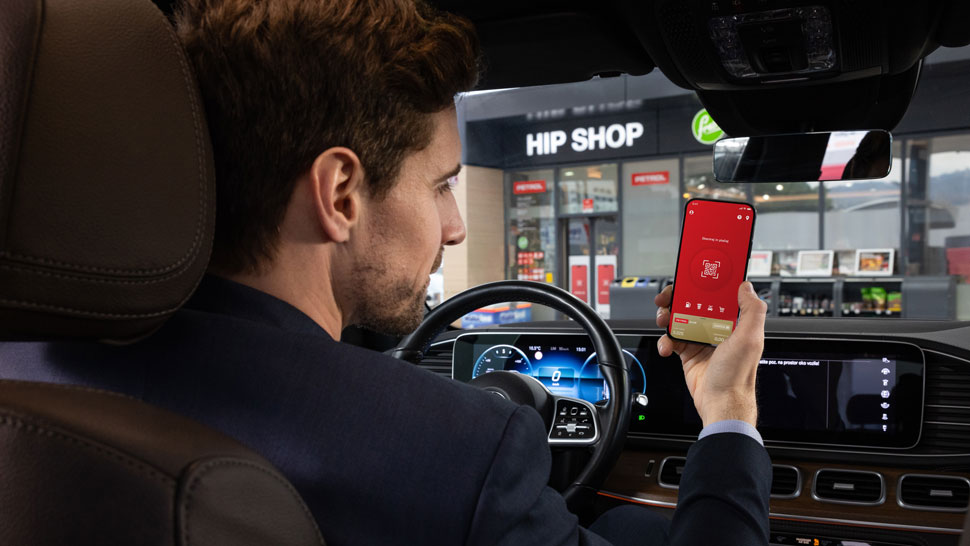 Moški v avtomobilu pred Petrolovo trgovino Hip Shop uporablja mobilno aplikacijo Petrol na telefonu.