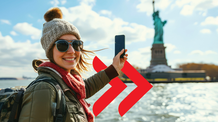 Na sliki je prikazano nasmejano dekle, ki stoji pred Kipom svobode v New Yorku. Dekle nosi sončna očala, kapo in šal ter v roki drži pametni telefon, s katerim si dela »selfie«. V ospredju levo je viden velik rdeč grafični simbol v obliki dvojne puščice, v ozadju pa nebo in nekaj stavb na obzorju.