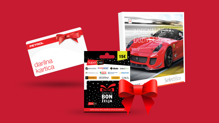 Na sliki je prikazano praznično darilno tematsko okolje z različnimi darilnimi karticami in boni na rdečem ozadju. Levo je darilna kartica Petrol z rdečo pentljo. Na desni strani je škatla SelectBox z motivom rdečega športnega avtomobila, ki predstavlja doživetja kot darilo. Spodaj na sredini je darilni bon za 15 evrov, okrašen s črno-rdečim dizajnom in rdečo pentljo. Celotna postavitev deluje praznično in predstavlja ideje za podarjanje daril.