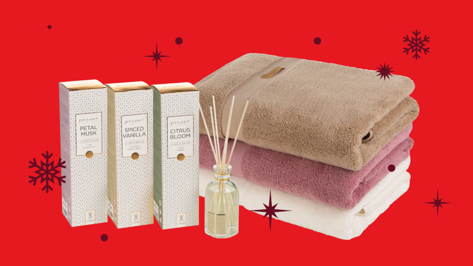 Na sliki je prikazano darilno predstavitveno okolje z mehkimi brisačami in dišavami za prostor. Na živahnem rdečem ozadju z dekorativnimi snežinkami so na levi strani postavljene tri škatlice dišav za dom z napisi Petal Musk, Spiced Vanilla in Citrus Bloom. Ob njih stoji steklenička z dišečo tekočino in lesenimi palčkami. Na desni strani je zložena bela, rožnata in bež brisača, pri čemer je zgornja brisača ovita s trakom. Slika deluje praznično in predstavlja izdelke za dom ter dobro počutje.