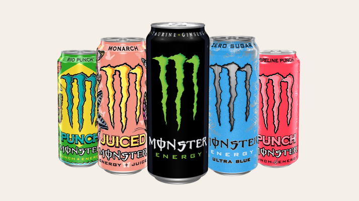 Na sliki je prikazan izbor pločevink energijske pijače Monster različnih okusov in barv, razporejenih ena ob drugi na svetlem ozadju.