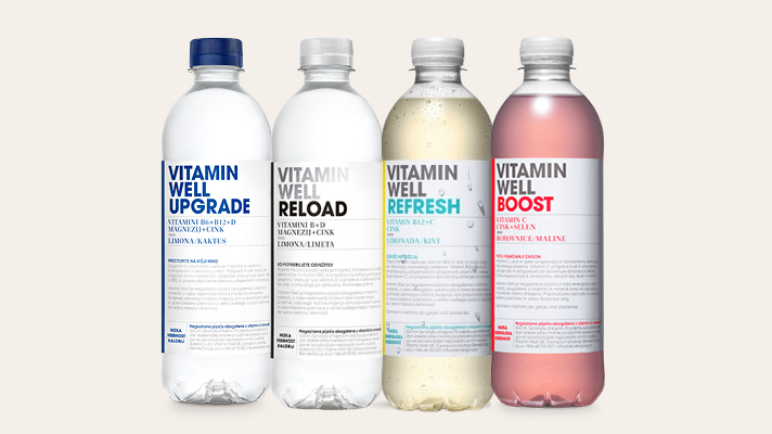 Na svetlem ozadju so prikazane štiri plastenke vitaminskih napitkov Vitamin Well: Upgrade, Reload, Refresh in Boost. Posamezni izdelki imajo različno barvno označene etikete in pokrovčke ter so postavljeni drug ob drugem.