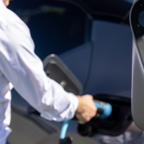 Oseba priklaplja kabel za polnjenje na električni avtomobil ob javni polnilnici.