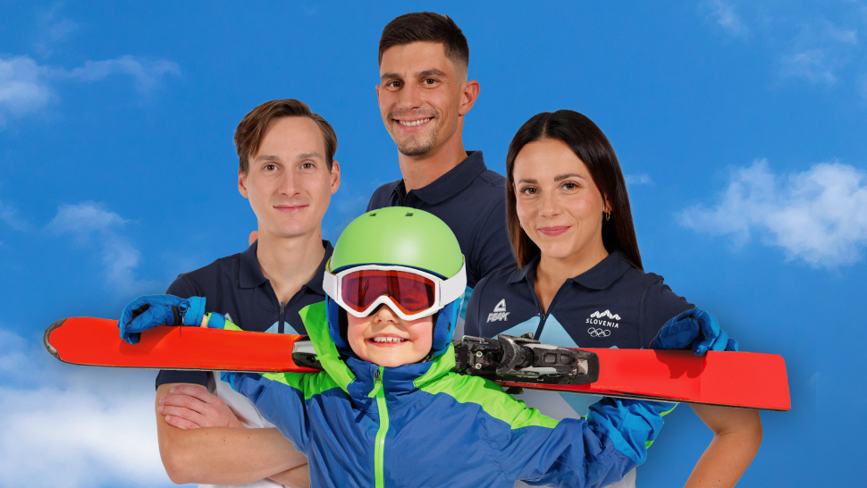 Na sliki je otrok v smučarski opremi s čelado in smučmi, pred tremi odraslimi v športnih oblačilih, postavljenimi na ozadju modrega neba.