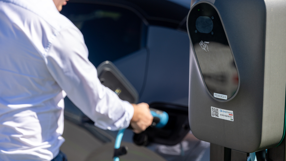 Oseba priklaplja kabel za polnjenje na električni avtomobil ob javni polnilnici.