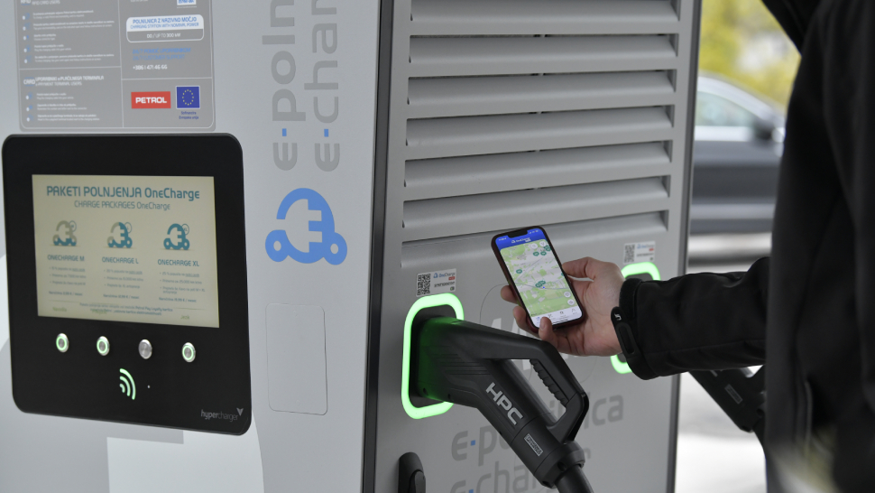 Oseba z mobilnim telefonom upravlja polnjenje električnega vozila na polnilnici.