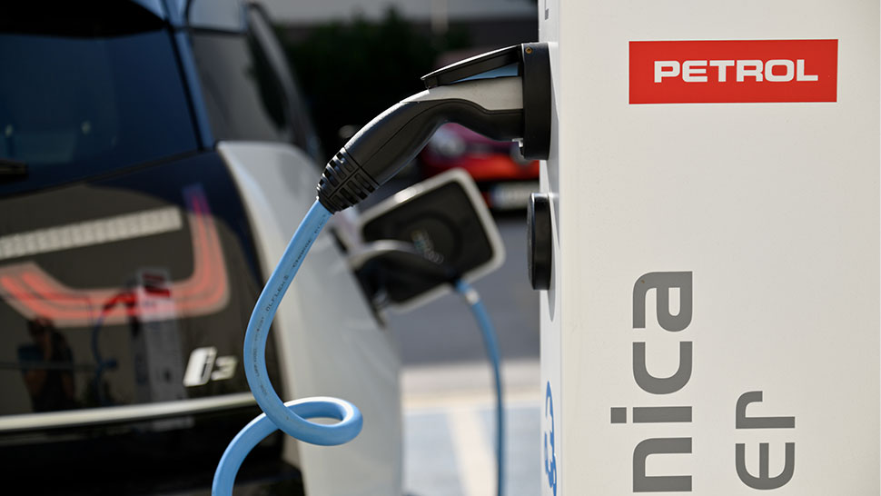 Električni avtomobil je priključen na polnilnico; v zgornjem delu slike je viden logotip Petrol.