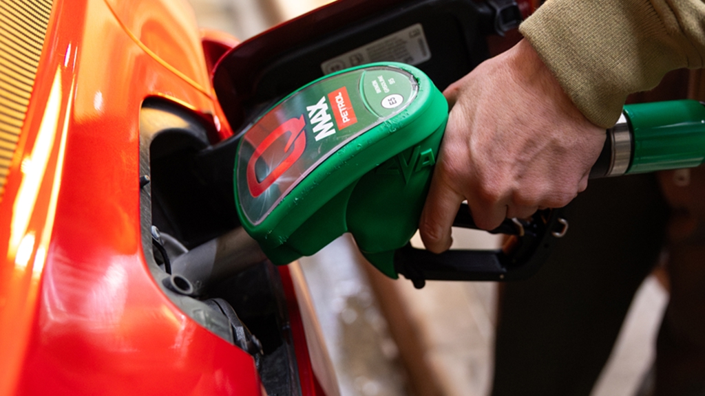 Roka drži zeleno ročko Petrol Q Max med točenjem goriva v oranžen avtomobil.