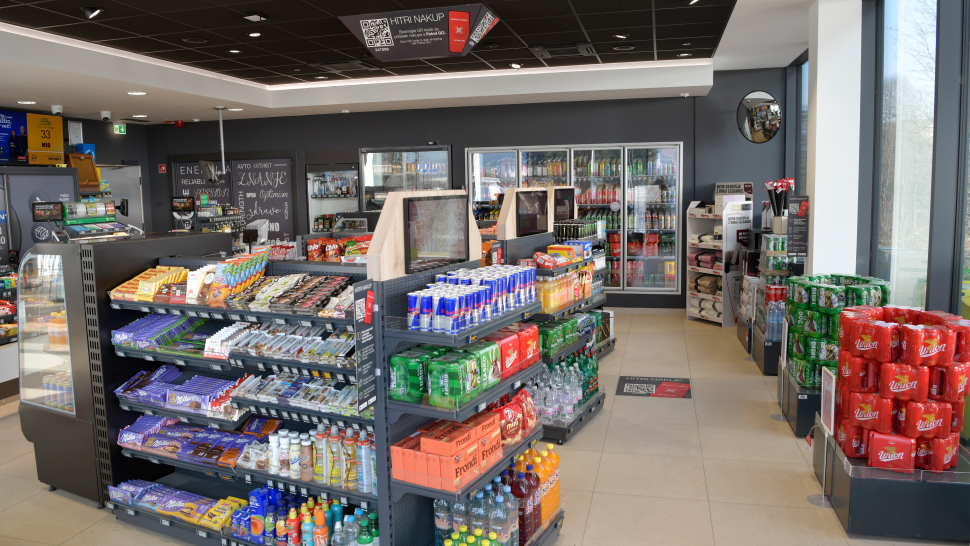 Notranjost Petrolove trgovine HipShop s policami, polnimi prigrizkov, pijač in osnovnih živil.