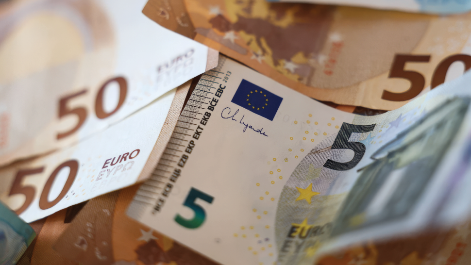 Na sliki so prikazani evrski bankovci različnih vrednosti, med njimi 5 in 50 evrov, v bližnjem posnetku z vidnimi evropskimi simboli in detajli zaščitnih elementov.