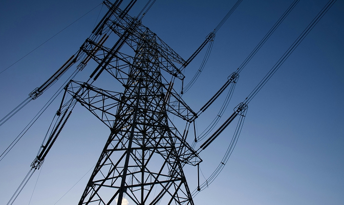 Električni daljnovod z visokonapetostnimi vodi se dviga proti modremu nebu.