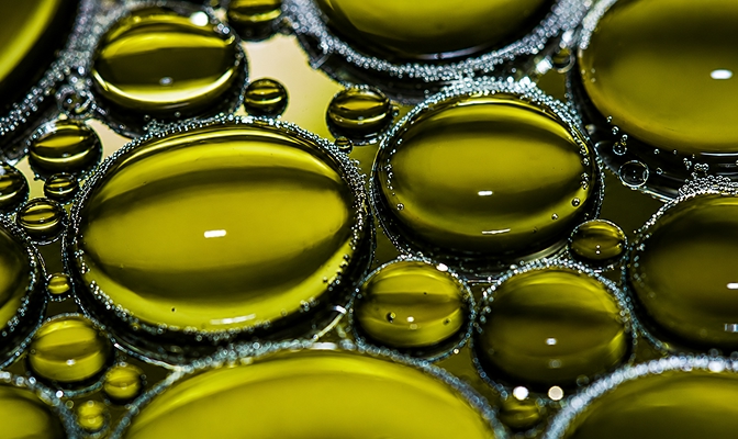 Kapljice kurilnega olja v makro posnetku ustvarjajo abstrakten vzorec zeleno-rumenih mehurčkov.