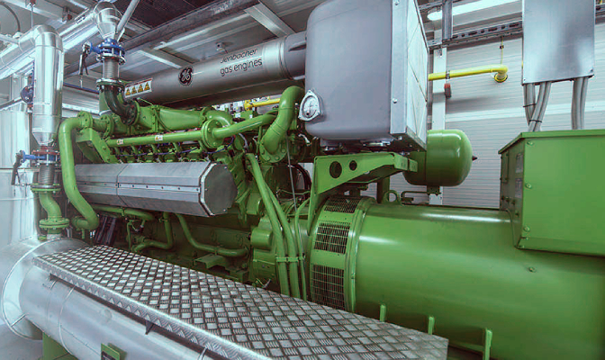 Na sliki je prikazan industrijski zeleni generator v strojnici, uporabljen za proizvodnjo električne energije