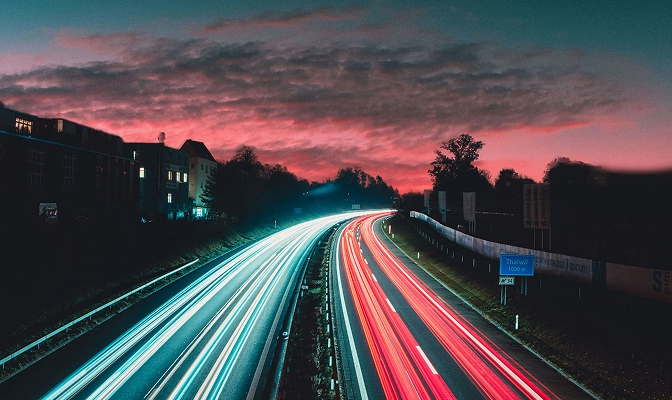 Avtocesta ob sončnem zahodu z dolgimi svetlobnimi sledmi vozil v obe smeri.