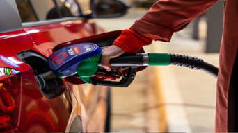 Roka drži točilno ročko Petrol Q Max med točenjem goriva v rdeč avtomobil.
