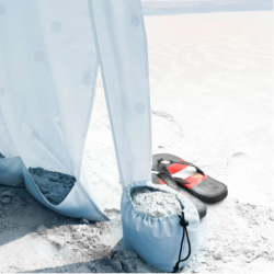Detajl plažnega paviljona z zaveso, obteženo z vrečko napolnjeno s peskom za stabilnost, postavljen na peščeni plaži.