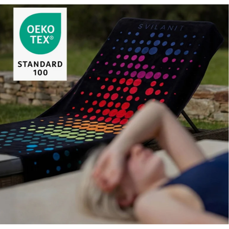 Ležalna brisača Svilanit, črna z barvnim pikčastim vzorcem, OEKO‑TEX Standard 100, uporaba ob bazenu.