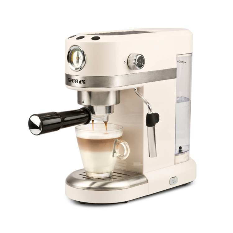 Espresso kavni aparat G3 Ferrari v kremni barvi z ročko za kavo, priprava latte napitka v steklenem kozarcu.