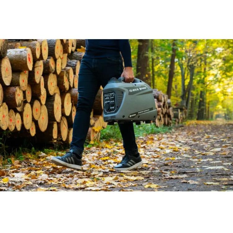 Prenosni bencinski inverter generator Fieldmann v uporabi na prostem, prenašanje po gozdni poti.