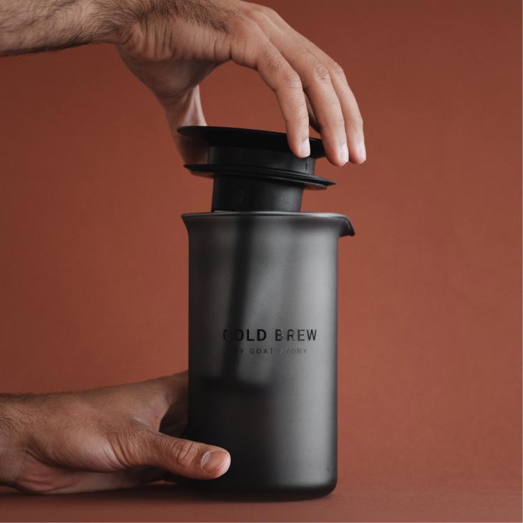 Goat Story Cold Brew, roka namešča pokrovček na vrč, mat črno ohišje in minimalističen dizajn.