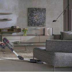 Baterijski sesalnik Hoover HFG10HX v uporabi pri sesanju pod kavčem z gibljivo talno krtačo.