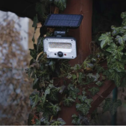 EMOS solarni LED reflektor nameščen na zunanji leseni konstrukciji, obdani z bršljanom, v večernem okolju