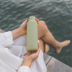 Oseba drži svetlo zeleno steklenico za vodo Equa ob vodi