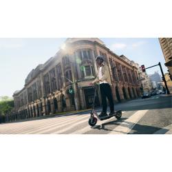 Segway F3 Pro E v mestnem okolju, vožnja čez prehod, urban arhitekturni ambient, črno‑siv skiro z rdečimi detajli.
