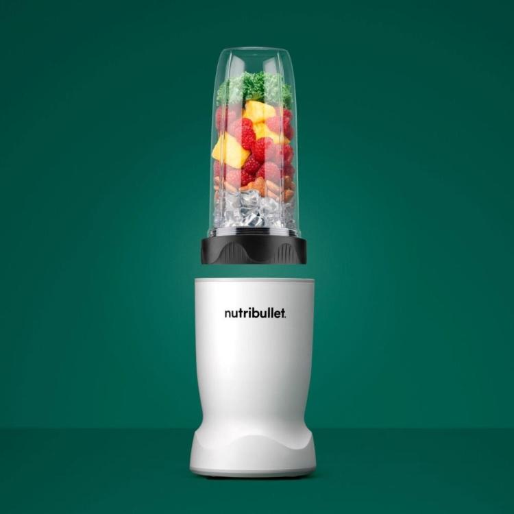 Nutribullet osebni blender z napolnjeno posodo (sadje, listnata zelenjava, led) na zeleni podlagi