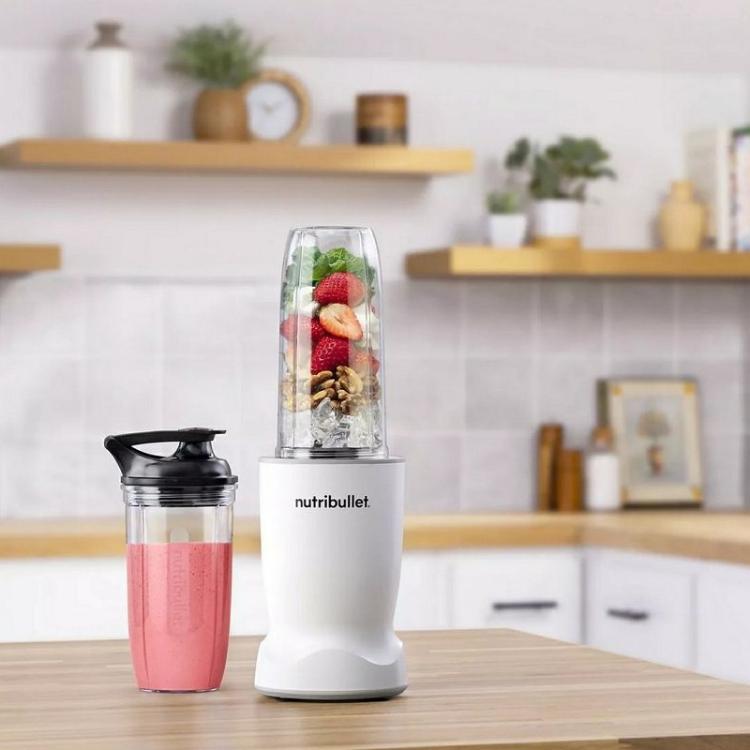 Nutribullet blender na kuhinjskem pultu z napolnjeno posodo (jagode, oreški, listnata zelenjava) in pripravljenim smoothijem