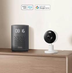 Pametna kamera Xiaomi C100, postavljena na omarici ob pametnem zvočniku, z združljivostjo za Amazon Alexa in Google Home.