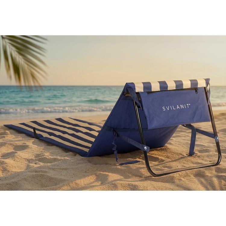 Plažna podloga z naslonjalom Svilanit v modro‑bež črtah, postavljena na pesku ob morju, pogled od zadaj z žepom za shranjevanje.