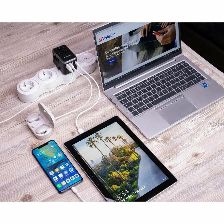 Verbatim adapter: potovalni adapter napaja prenosnik, telefon in tablico prek več USB priklopov na delovni mizi.