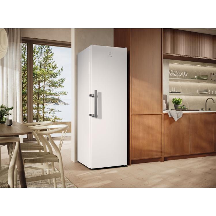 Enovratni hladilnik Electrolux, bel, postavljen v moderni kuhinji ob jedilni mizi in lesenih elementih.