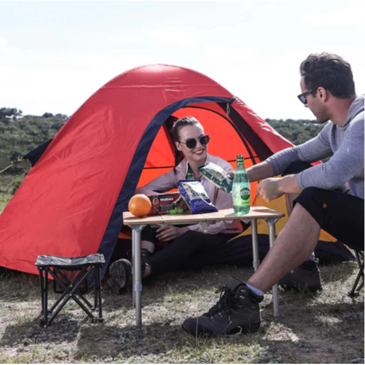 Zložljiva kamping mizica v uporabi pri kampiranju ob šotoru, primerna za piknik in kamping.